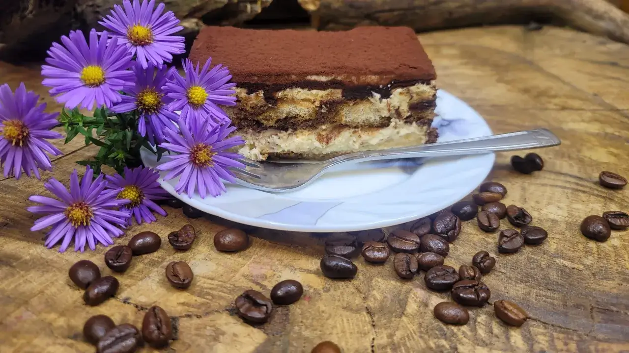 Pyszny kawałek tiramisu, ozdobiony fioletowymi kwiatami i ziarnami kawy, wygląda jak najlepsze tiramisu.