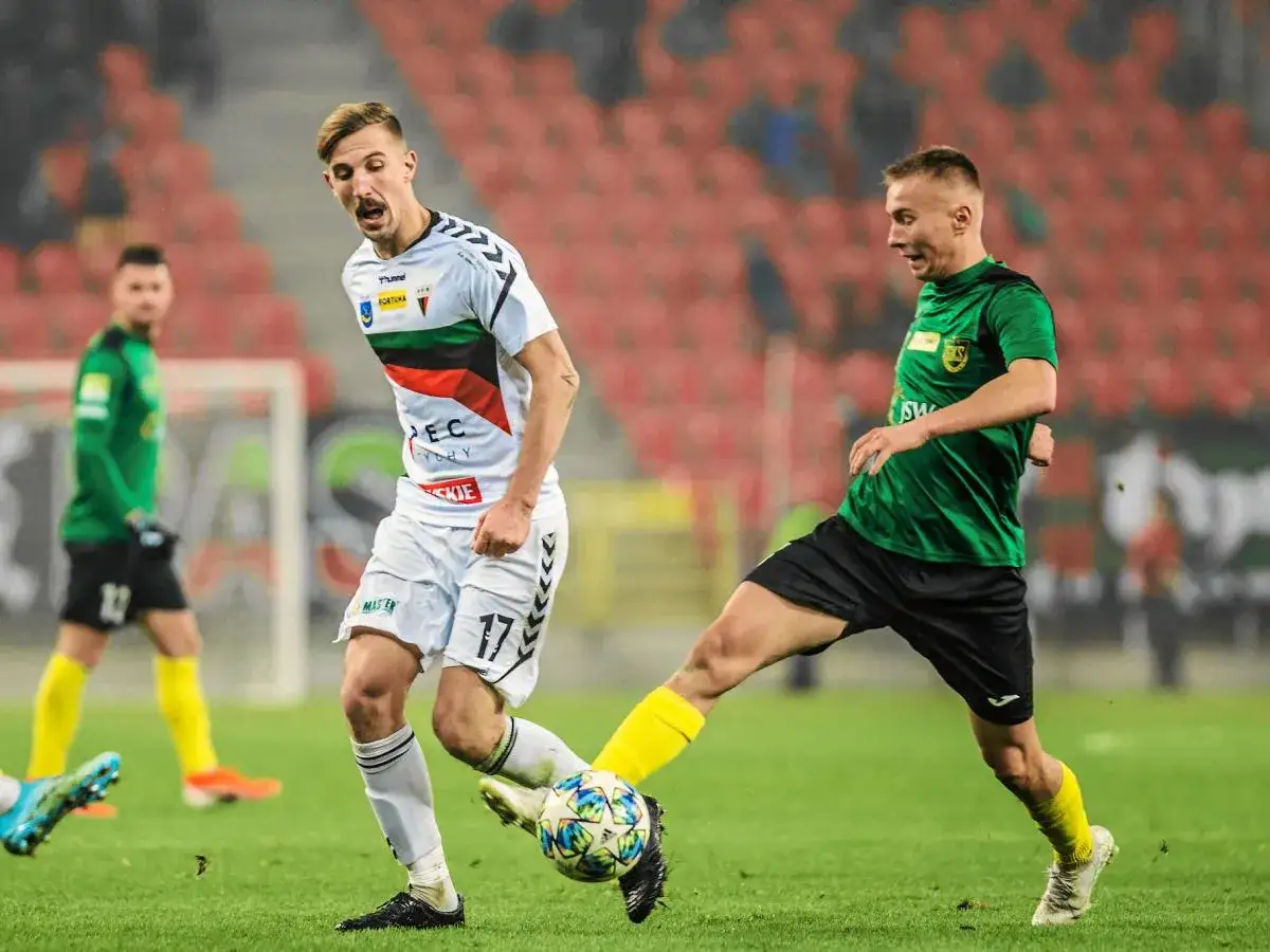 Piłkarze walczą o piłkę, jeden w białej koszulce z numerem 17, drugi w zielonej. Stawka jest wysoka – kto wchodzi do ekstraklasy?