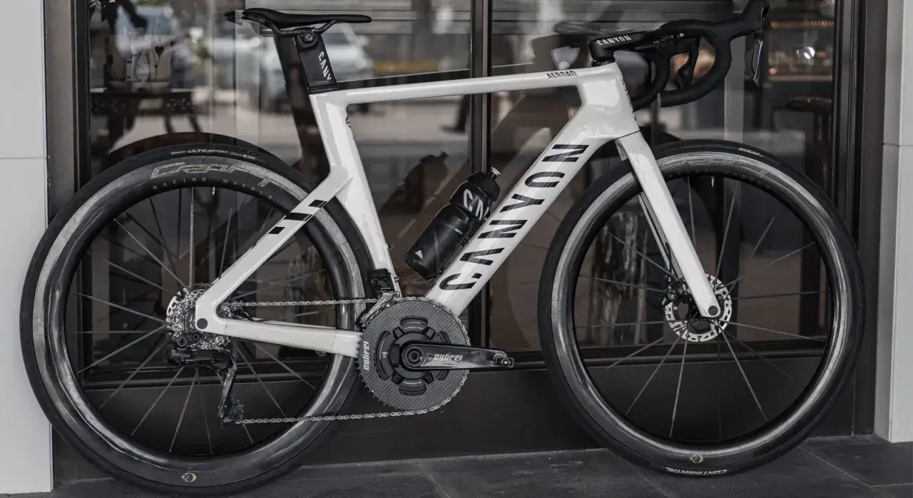 Biały rower szosowy Canyon Aeroad, prawdopodobnie najlżejszy rower na świecie, z czarną butelką i napędem.