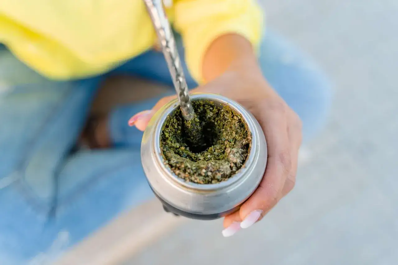 Dłoń trzyma naczynie z yerba mate, do którego nalewana jest gorąca woda. Tak działa yerba mate, napój pełen energii.