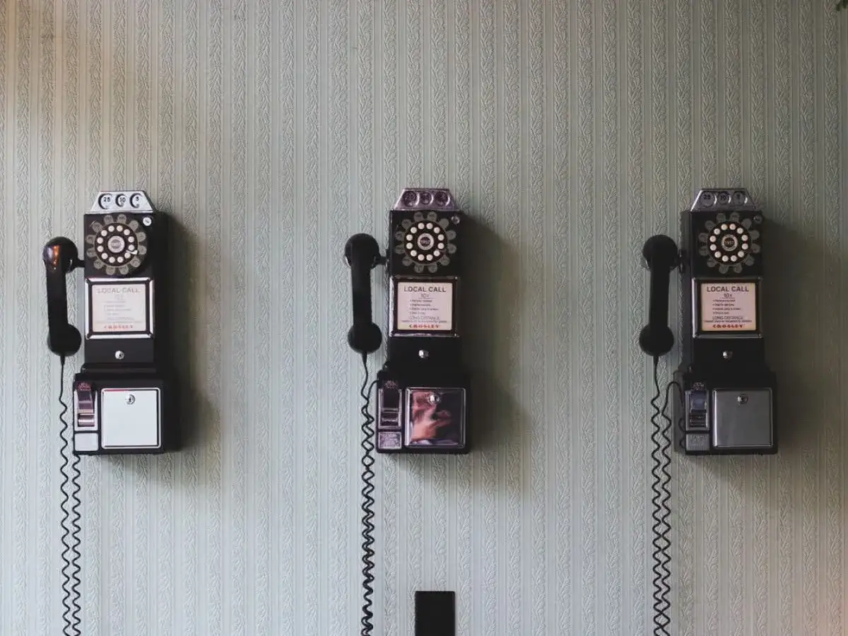 Trzy zabytkowe telefony na ścianie, jakby z czasów, kiedy Bell wynalazł telefon.