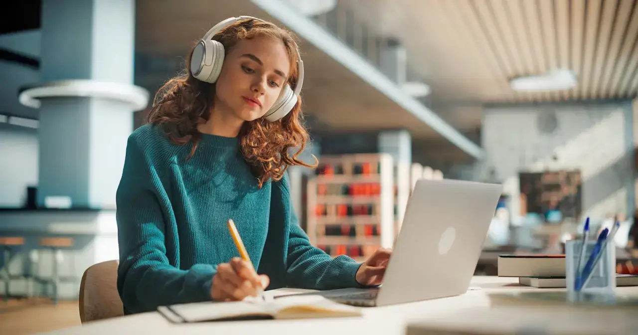 Dziewczyna w słuchawkach uczy się z laptopa, zastanawiając się, czy darmowe treści celebryty są lepsze niż jego płatny kurs premium.