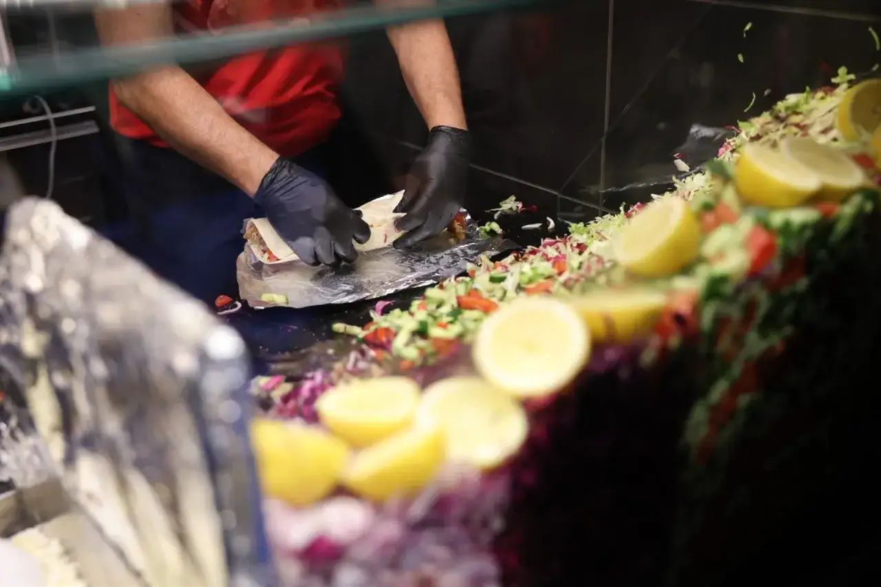 Ręce w czarnych rękawiczkach zwijają świeżego kebaba. Obok kolorowa sałatka i cytryny. Zastanawiasz się, ile kebabów dziennie można sprzedać?