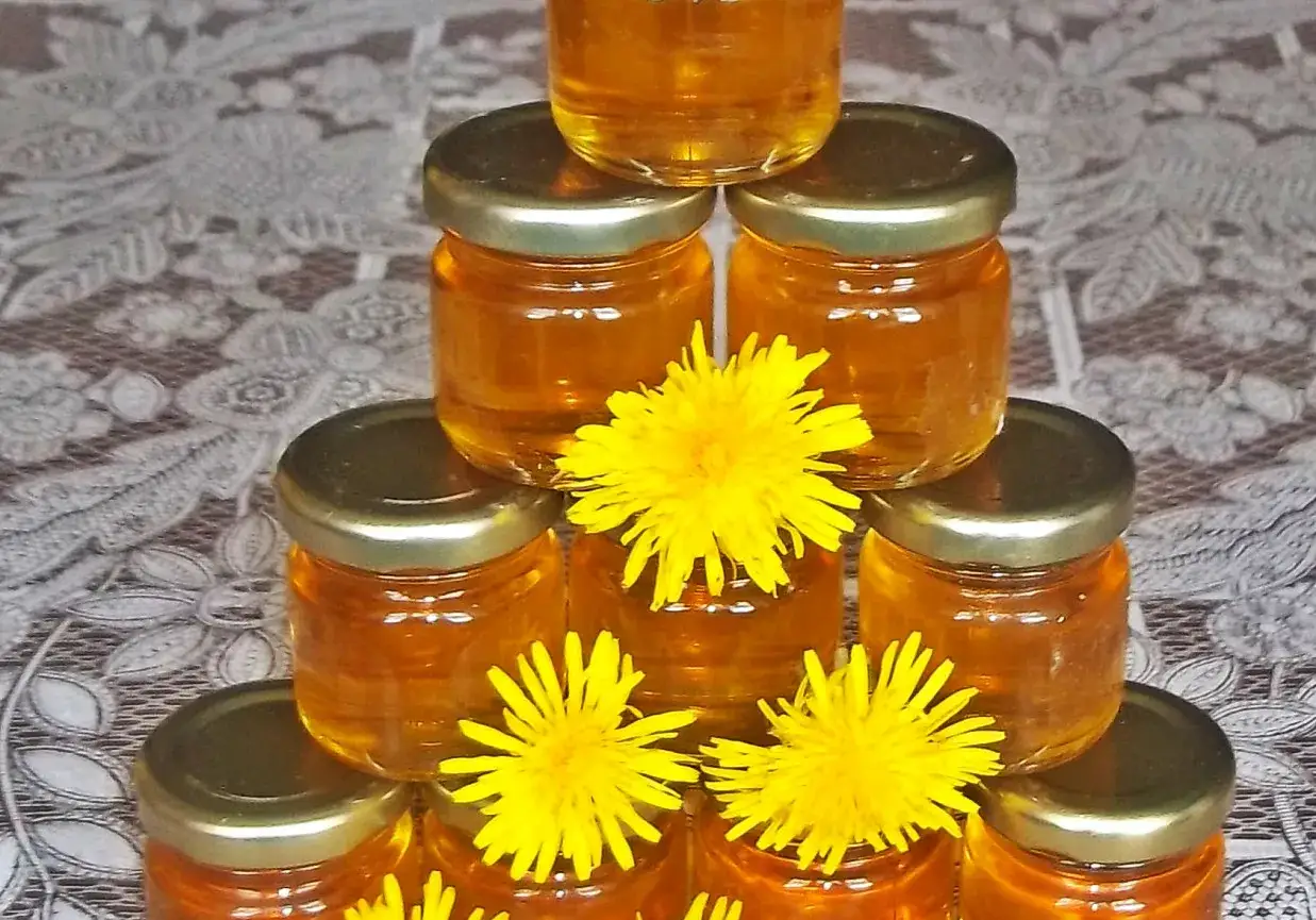 Słoiczki ze złotym syropem z mniszka, ozdobione świeżymi kwiatami mniszka.