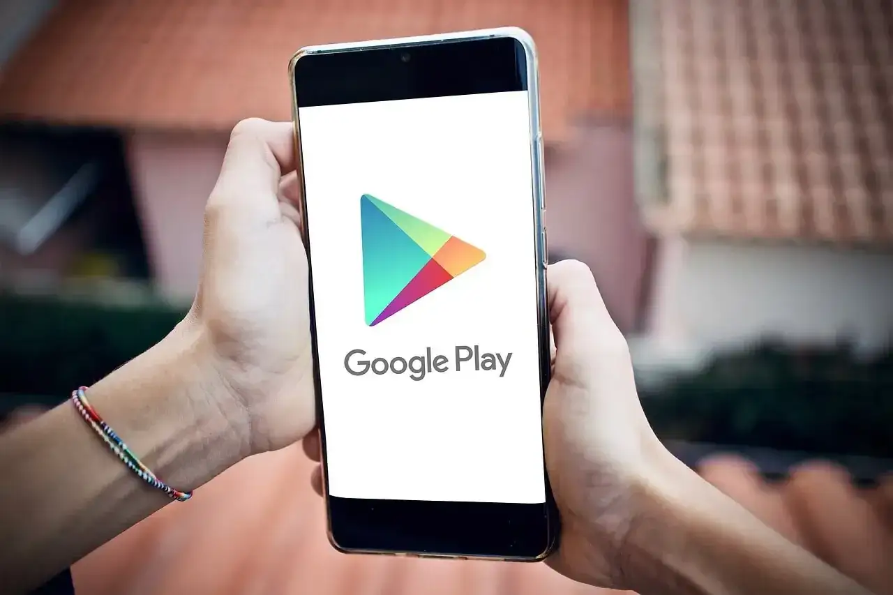 Ręce trzymają smartfon z logo Google Play. Zastanawiasz się, jak pobierać płatne aplikacje za darmo na Androida?