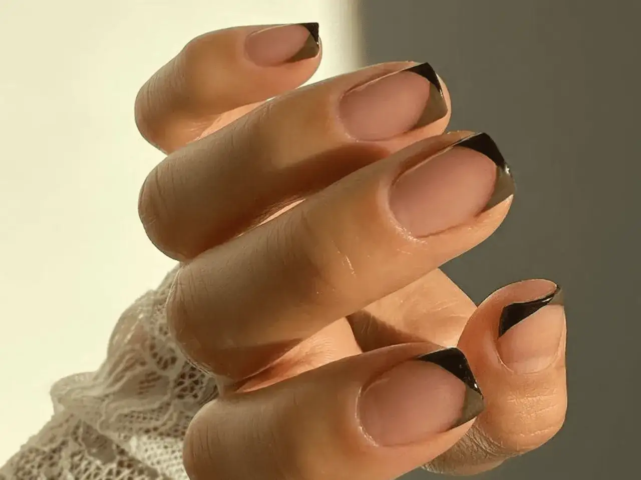 Dłoń z kwadratowymi paznokciami w stylu french manicure z czarnymi końcówkami. Eleganckie i nowoczesne french paznokcie kwadratowe.