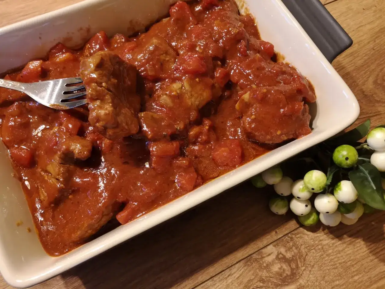 A fork lifts a piece of tender polędwiczki w sosie sojowym z pomidorami z białej brytfanny.