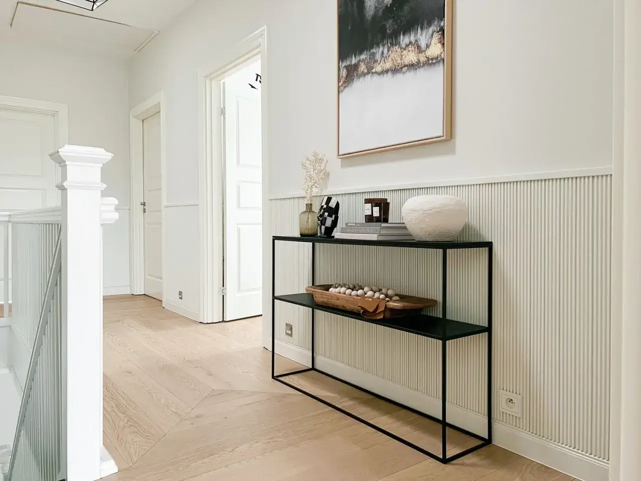 Nowoczesny korytarz z panelami ściennymi, kt&oacute;re przypominają, jak zrobić lamele. Na konsoli dekoracje i obraz.