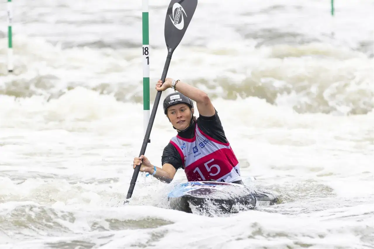 Zawodniczka w kajaku, w kasku i kamizelce z numerem 15, walczy z rwącym nurtem. To emocjonujące kajakarstwo na igrzyskach olimpijskich.