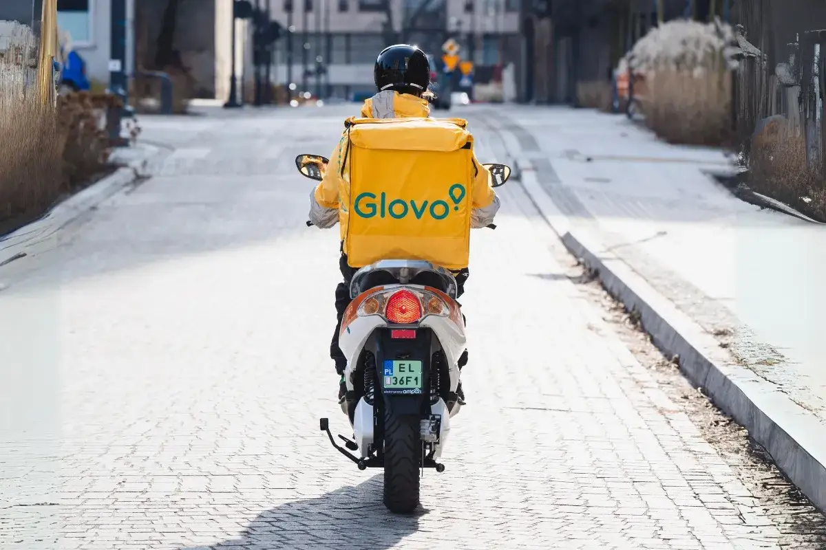 Kurier Glovo na skuterze w żółtej kurtce z logo. Zastanawiasz się, ile zarabia pracownik Glovo?