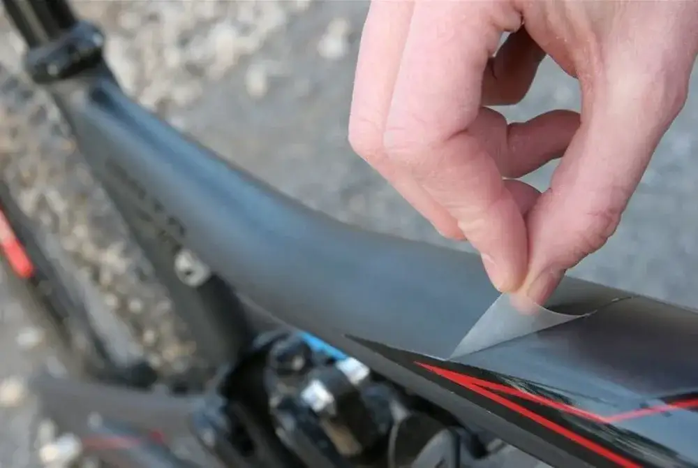 Dłoń przykleja przezroczystą folię ochronną na ramę roweru, zapewniając jej zabezpieczenie przed zarysowaniami.