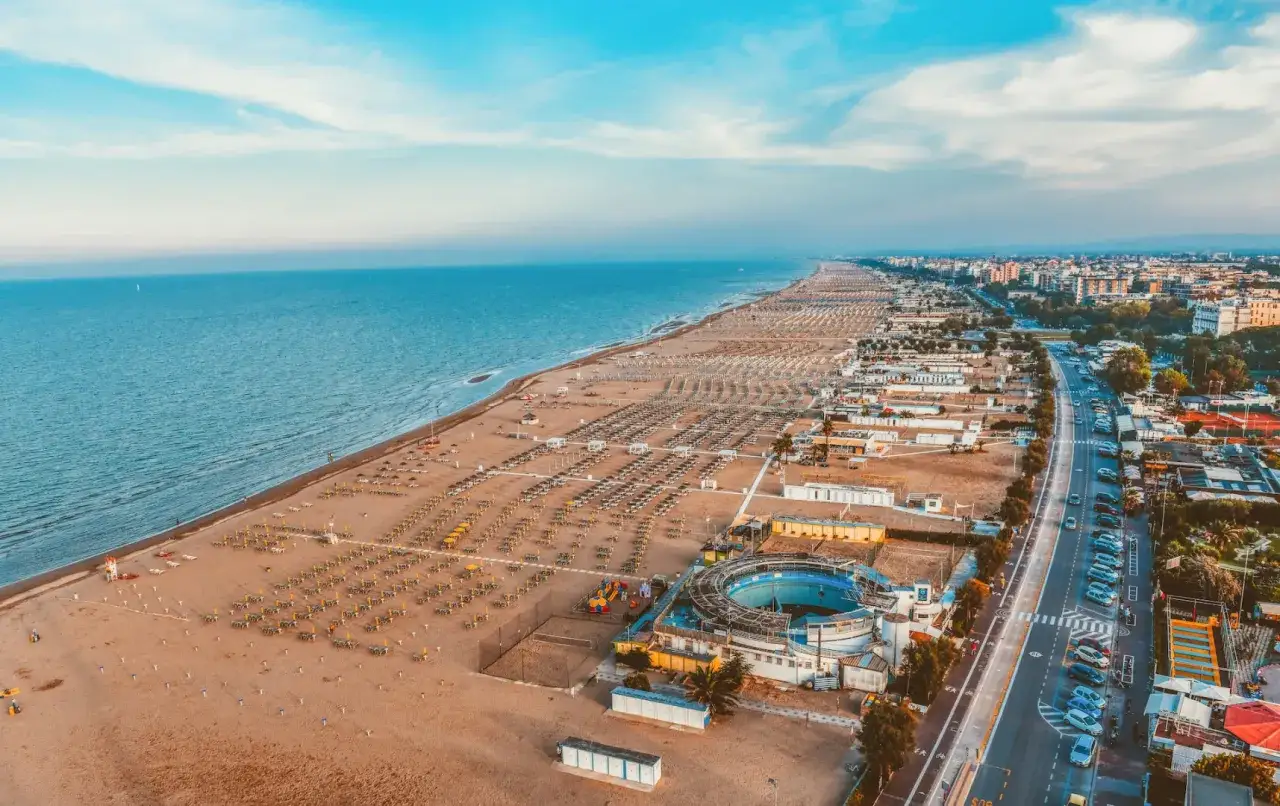 Szeroka, piaszczysta plaża w Rimini, pełna leżaków i parasoli, z widokiem na spokojne morze i miasto. Czy Rimini jest bezpieczne? Wygląda na spokojne i przygotowane na turystów.