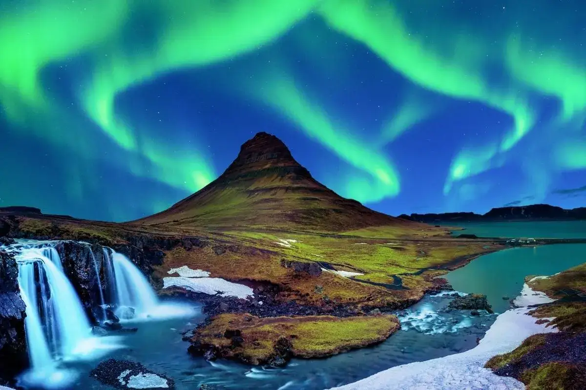 Górzysty krajobraz Islandii z wodospadem i zorzą polarną na nocnym niebie. Idealne miejsce, by zastanowić się, kiedy lecieć na Islandię, by zobaczyć takie cuda.