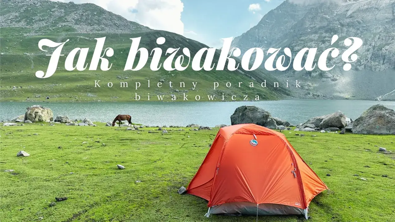 Pomarańczowy namiot na zielonej łące nad jeziorem, idealne miejsce na biwak. W tle g&oacute;ry i koń.