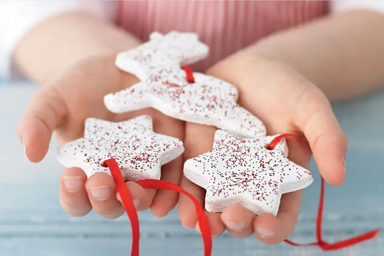 Dziecko trzyma w dłoniach ozdoby z masy solnej: renifera i dwie gwiazdki, posypane brokatem.