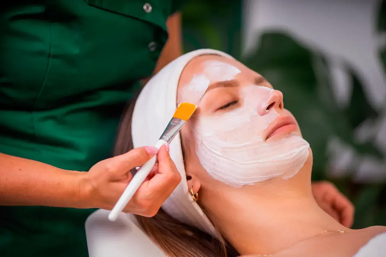 Kosmetyczka nakłada maskę na twarz klientki. To część jej pracy, kod zawodu kosmetyczka.