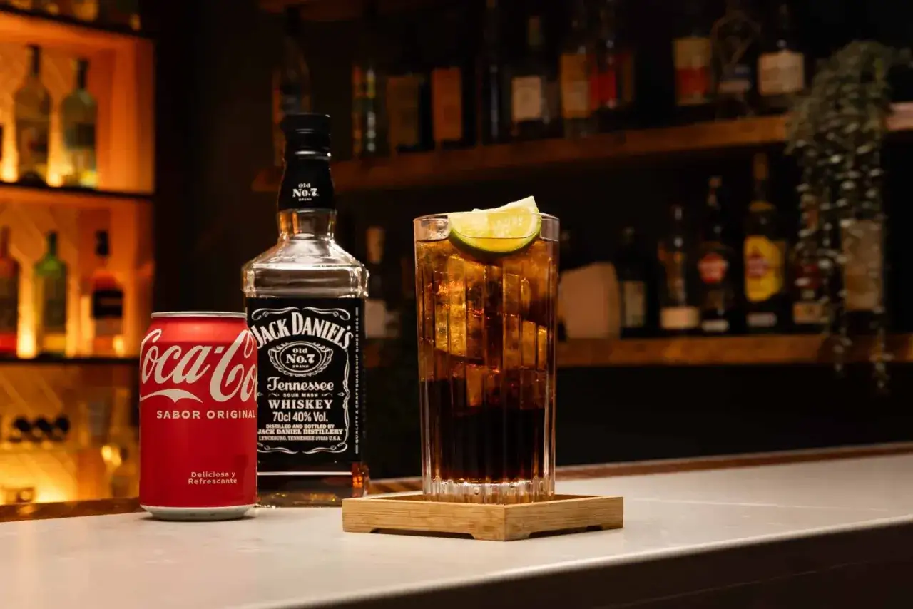 Idealne proporcje whisky z colą: szklanka drinka z lodem, limonką, obok puszka Coca-Coli i butelka Jack Daniel's.