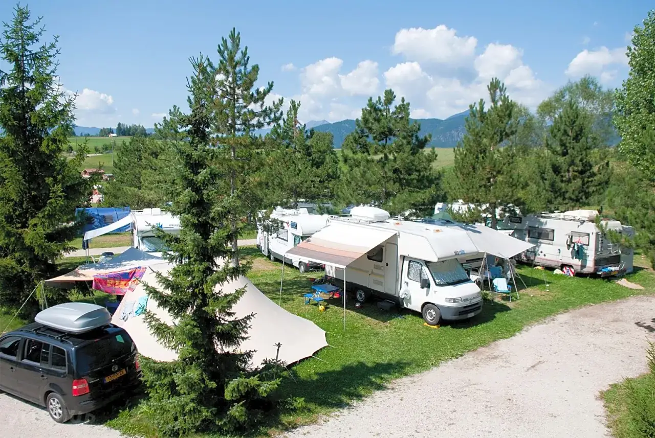 Malowniczy **dolomity camping** z kamperami, namiotami i samochodami pod drzewami.