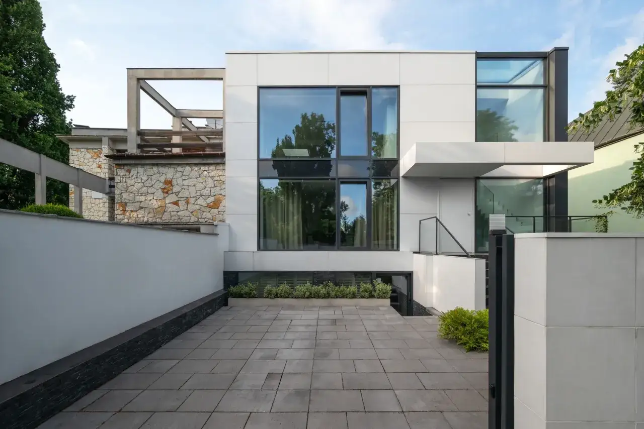 Nowoczesny dom kostka projekty: biała bryła z dużymi oknami, kamienna ściana i betonowe elementy tworzą minimalistyczną kompozycję.