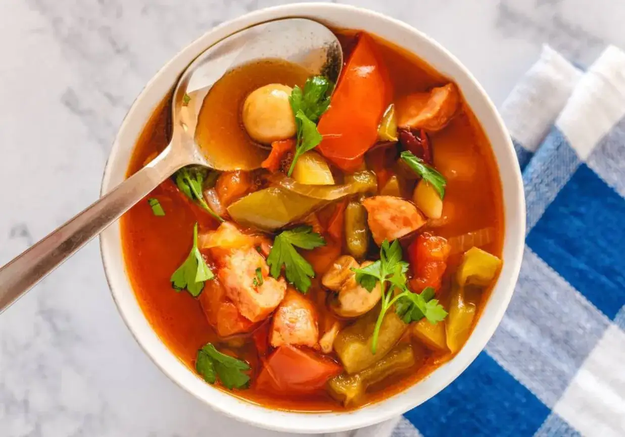 Gorące leczo z kiełbasą, papryką i pomidorami, ozdobione natką pietruszki, gotowe do podania.