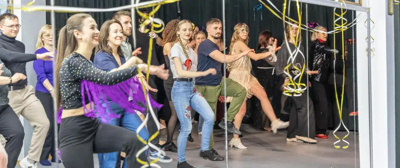 Grupa ludzi uczy się tańca towarzyskiego, wesoło poruszając się w rytm muzyki.