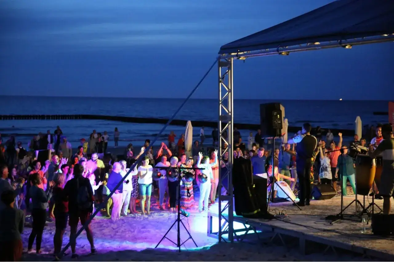 Koncert na plaży, tłum bawi się przy muzyce. To właśnie takie miejsca tworzą atmosferę najbardziej imprezowych miast nad morzem.