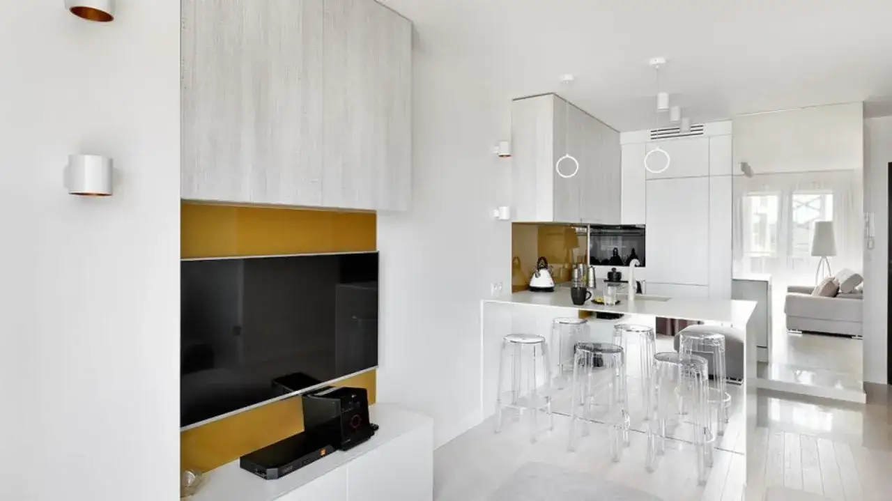 Nowoczesne wnętrze, jak urządzić małe mieszkanie 35 m. Biała kuchnia z wyspą, przezroczyste hokery, TV.