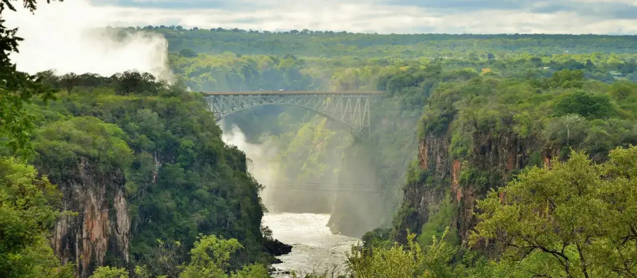 Most impressive zimbabwe atrakcje: Most nad Wodospadami Wiktorii, otoczony bujną zielenią i mgiełką wodną.