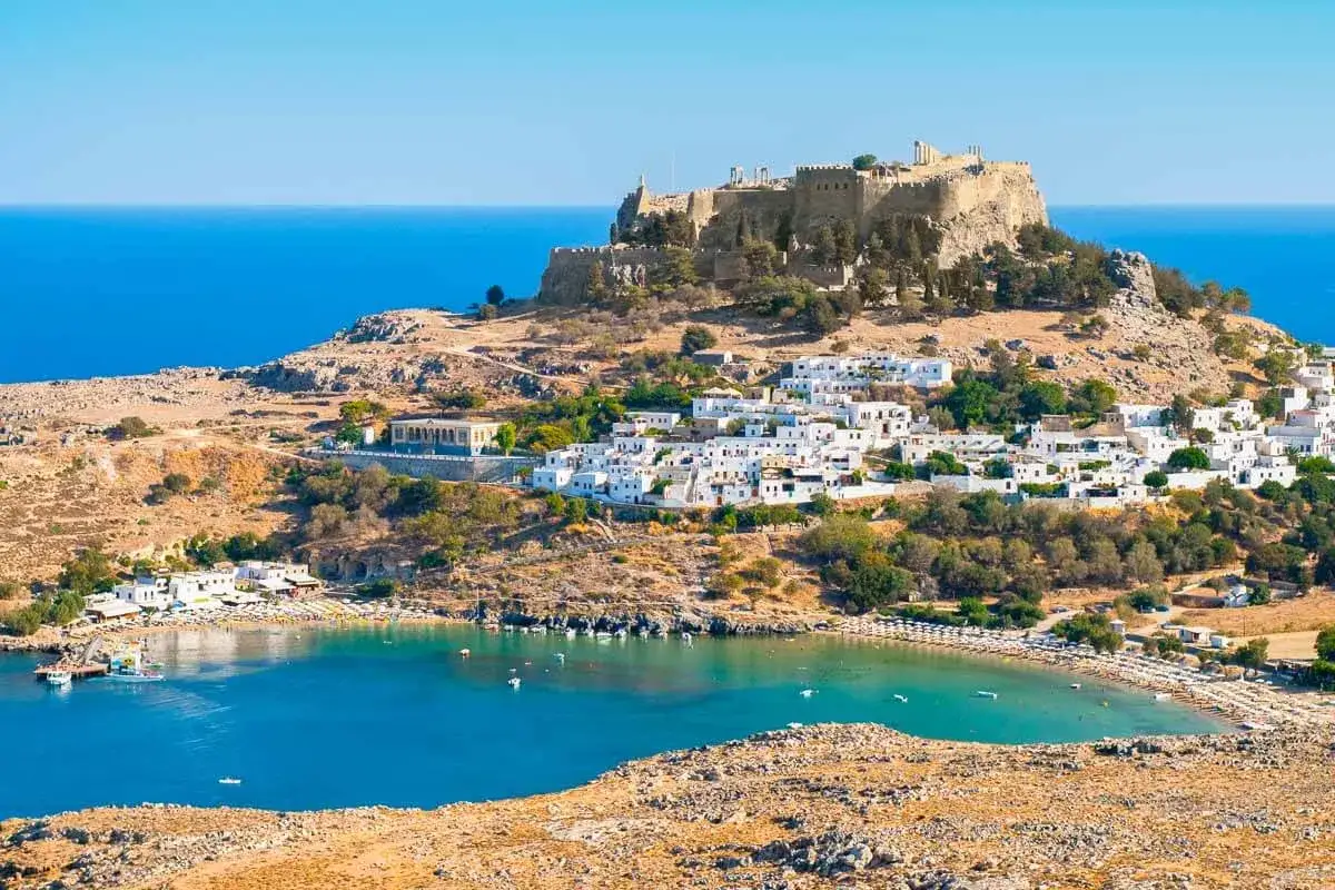 Malownicze białe miasteczko na wzg&oacute;rzu, zamek Akropol i turkusowa zatoka. To widok z najcieplejszej wyspy greckiej, idealnej na wakacje.