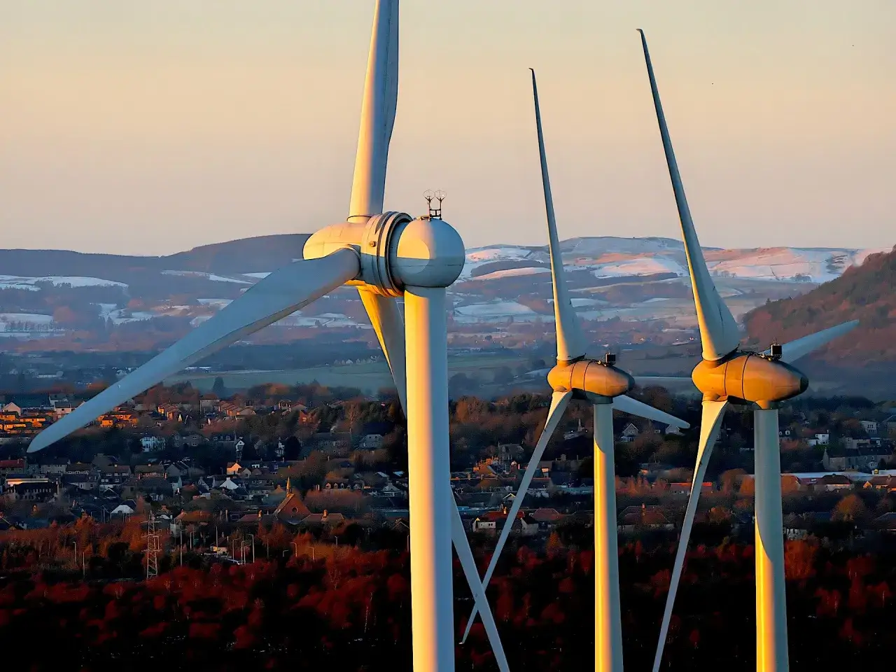 Trzy wiatraki na tle zachodzącego słońca nad miasteczkiem. Czysta energia z wiatru zasila przyszłość.