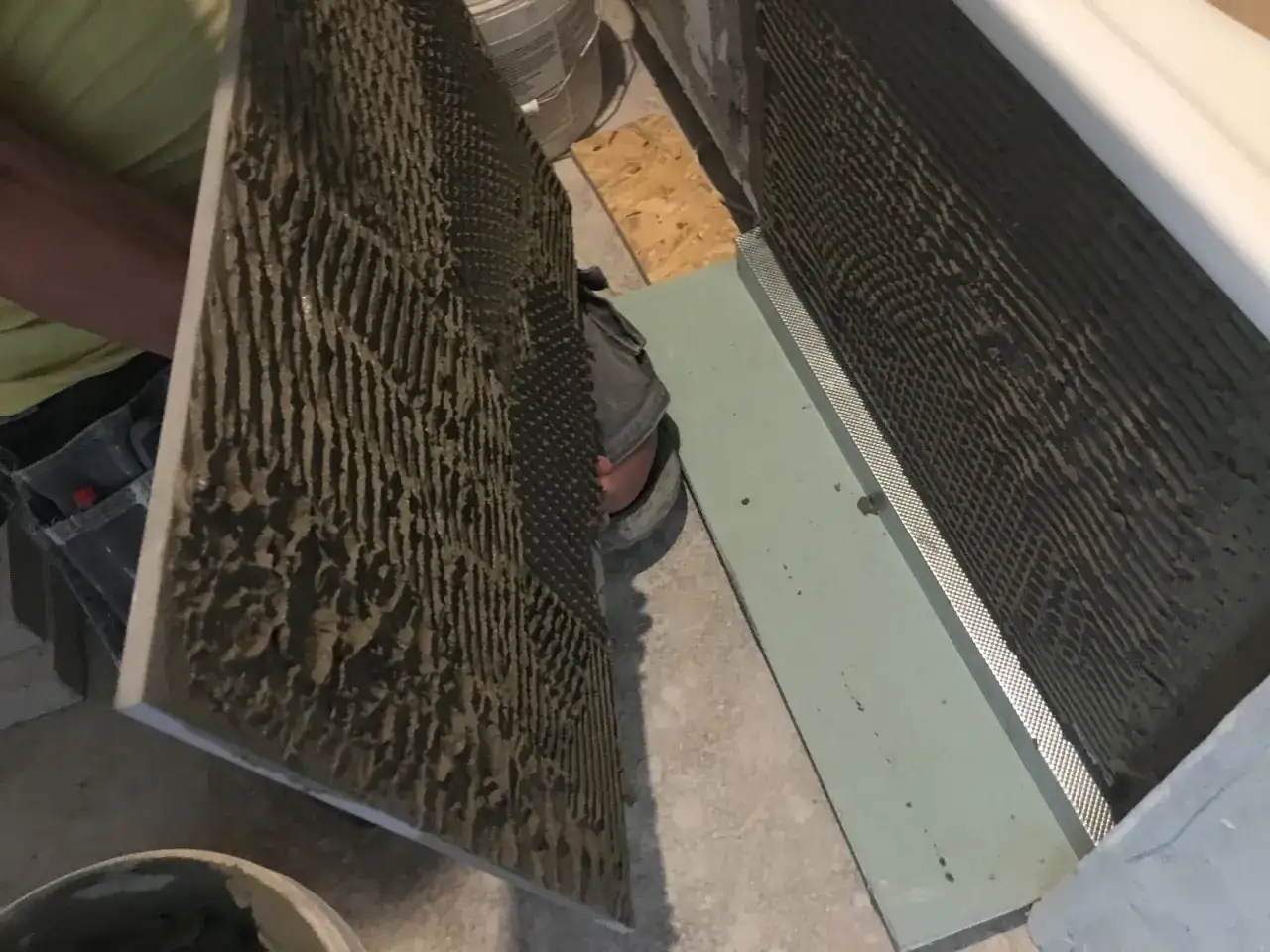 Płytkarz przygotowuje się do montażu, sprawdzając dopuszczalną grubość kleju pod płytki na dużej płycie.