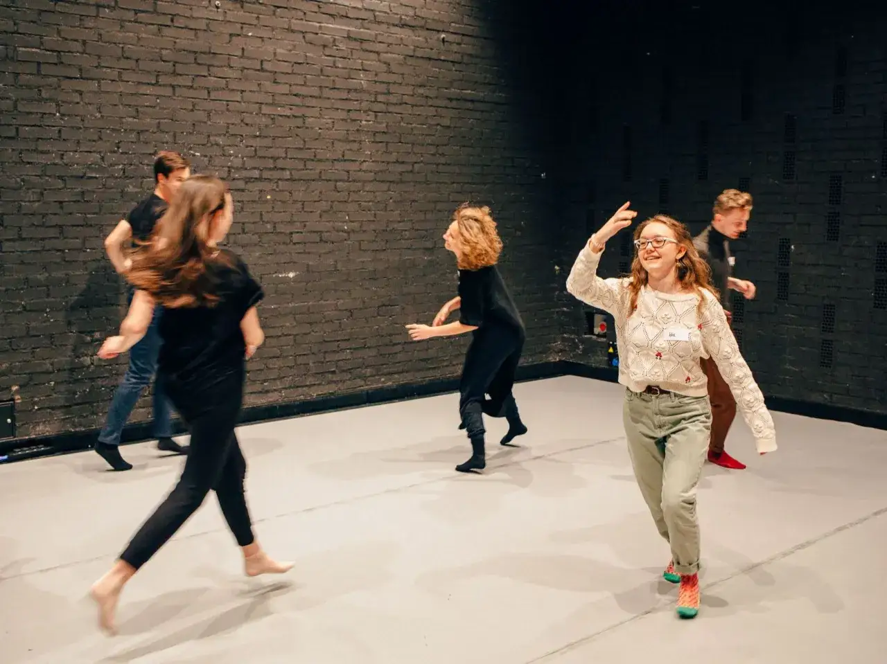 Choreograf kieruje grupą tancerzy podczas pr&oacute;by. Wszyscy poruszają się w rytm, tworząc dynamiczną kompozycję.