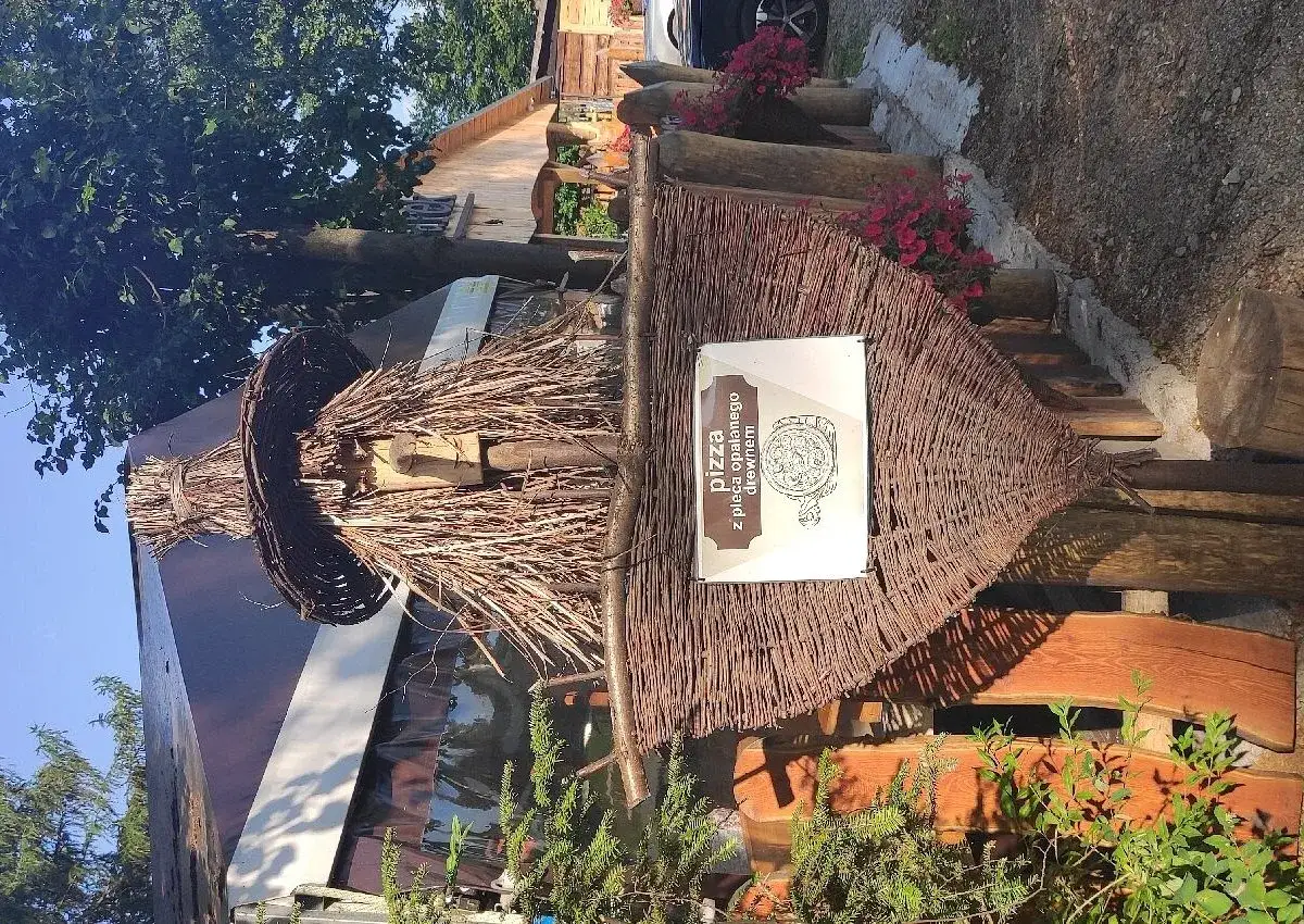 Restauracja Gwarek Polańczyk zaprasza na pizzę opalaną drewnem. Widać tu rustykalny wystrój i zielone otoczenie.