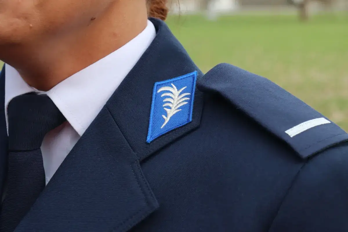 Szczegół umundurowania policjantów: granatowa marynarka, biała koszula, krawat i niebieska naszywka z białym liściem.