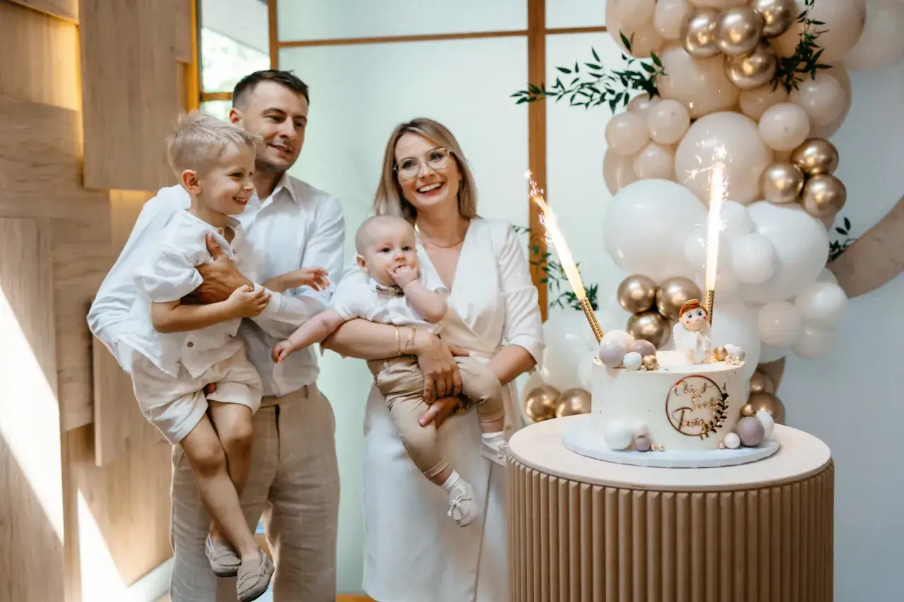 Rodzina świętuje chrzciny. Zastanawiasz się, ile bierze fotograf za chrzciny? Tutaj rodzice z dziećmi pozują do zdjęcia z tortem i fajerwerkami.