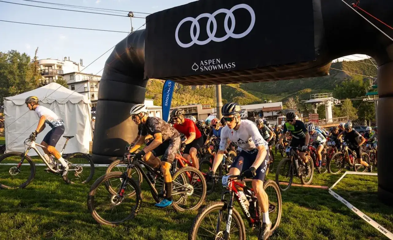 Kolarze startują w g&oacute;rskich rajdach rowerowych dla amator&oacute;w pod bramą z logo Audi.