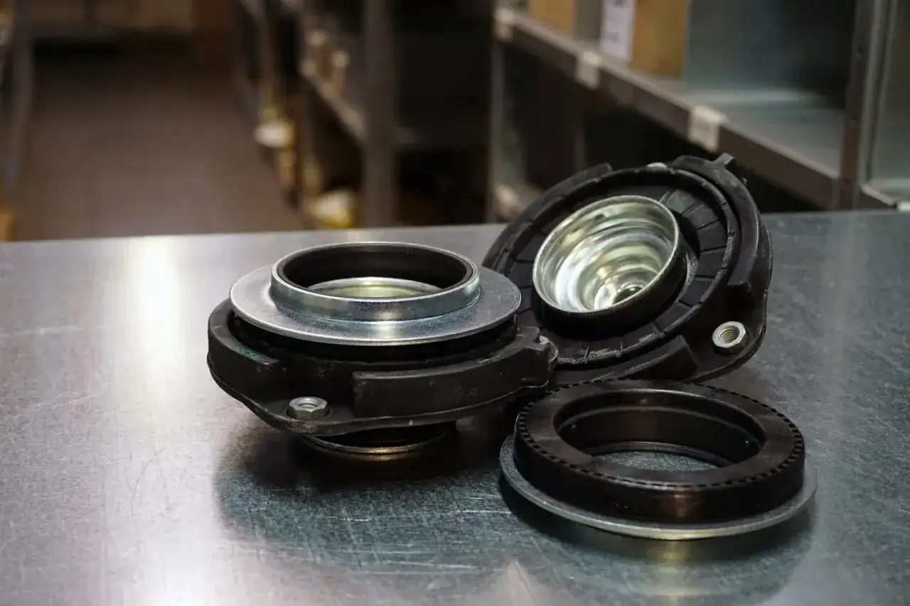 Zużyte łożysko amortyzatora objawy: stuki, luzy, nier&oacute;wna jazda. Widoczne części zamienne.