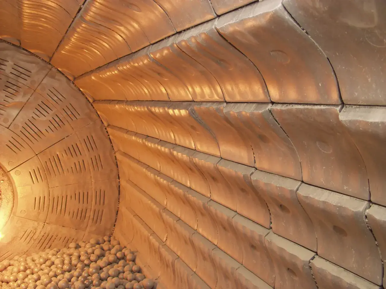 Wnętrze młyna kulowego z okładziną ceramiczną, gdzie powstaje półprodukt do produkcji cementu portlandzkiego. Widać tam kulki mielące i faliste kształty okładziny.