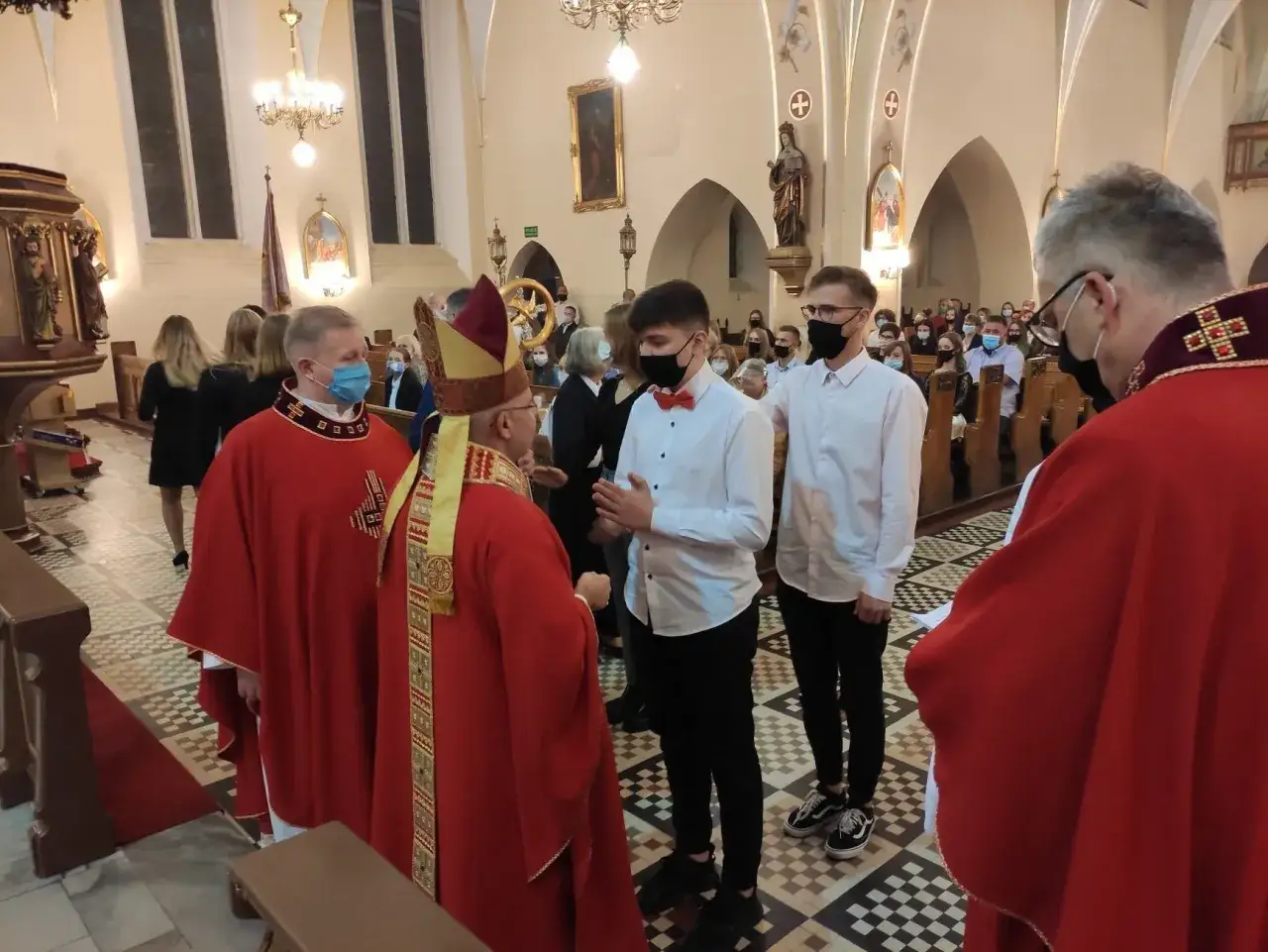 Biskup udziela sakramentu bierzmowania młodym mężczyznom. Ceremonia odbywa się w kościele, a koszt bierzmowania dla dorosłych jest zazwyczaj symboliczny.