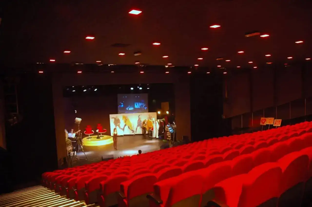 Widok na salę kinową Teatru Capitol z czerwonymi fotelami. Na scenie przygotowania do spektaklu, widać ekran i manekiny z ubraniami.