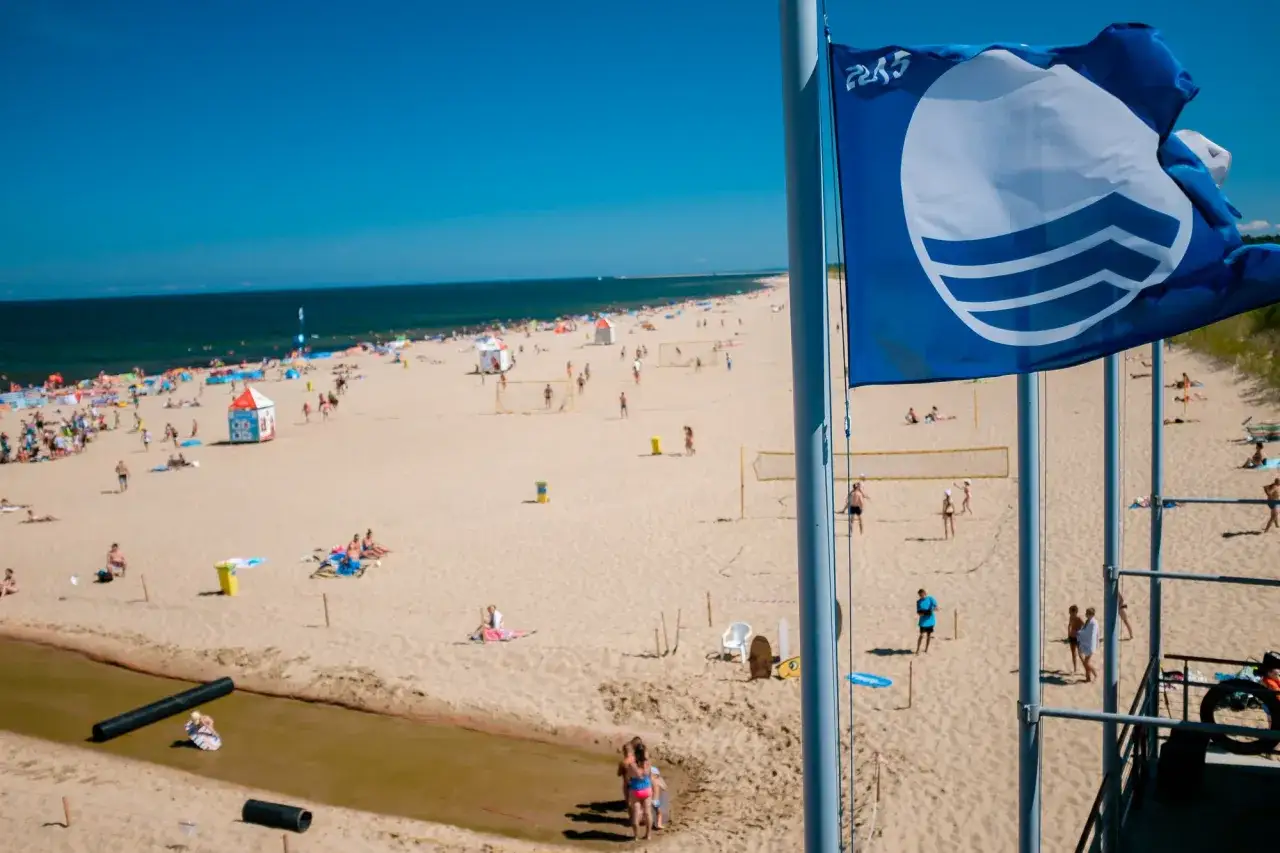 Błękitna flaga na plaży sugeruje, że morze czarne jest czyste i bezpieczne dla kąpiących się. W tle widać tłumy ludzi i siatkówkę plażową.
