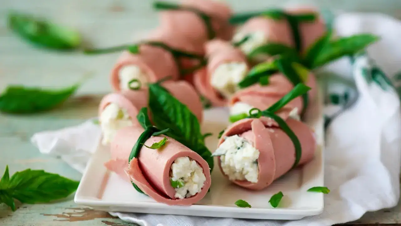 Roladki z szynki konserwowej nadziewane serem i szczypiorkiem, ozdobione listkami bazylii.