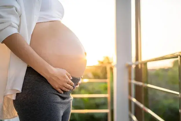 kobieta w ciąży dotykająca brzucha na tle zachodu słońca