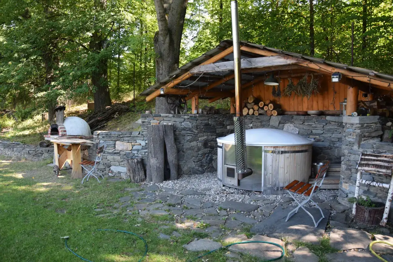 Agroturystyka bac&oacute;wka Giemzik&oacute;w: drewniana balia z piecem, piec chlebowy i kamienne mury w otoczeniu zieleni.