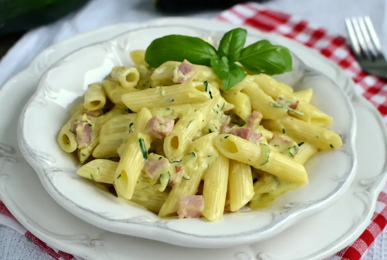 Penne w kremowym sosie z boczkiem i cukinią, ozdobione listkiem bazylii. Pyszna carbonara z cukini.