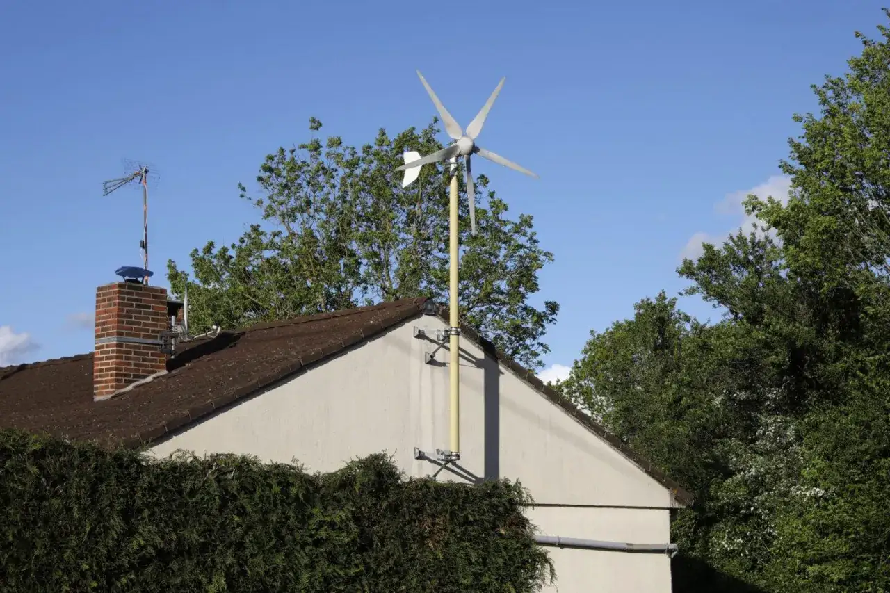 Mała elektrownia przydomowa z turbiną wiatrową na maszcie, zamontowana na ścianie domu.