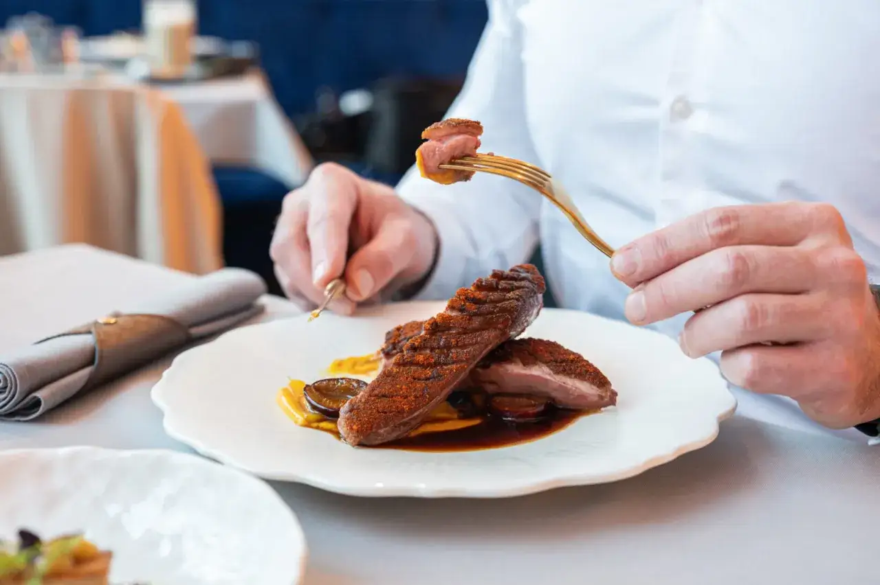 Eleganckie danie z kaczki na talerzu, idealne jako przepis na obiad jak z restauracji. Złoty widelec podnosi kawałek mięsa.