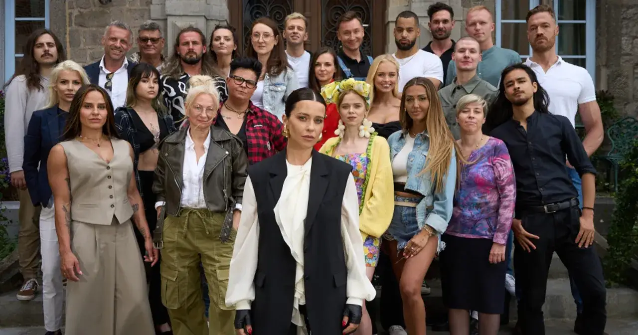 Grupa uczestnik&oacute;w, wśr&oacute;d kt&oacute;rych są potencjalni zdrajcy, pozuje do zdjęcia przed kamiennym budynkiem.