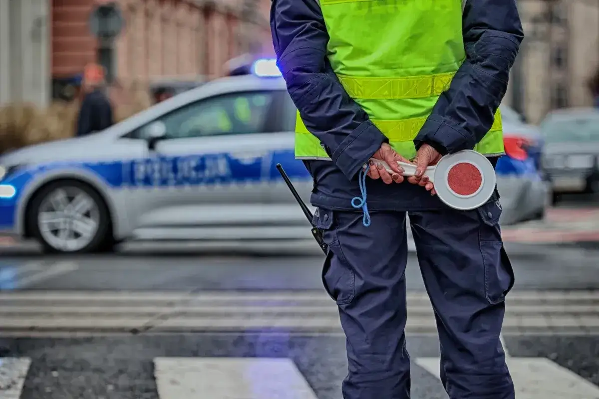 Policjant z lizakiem i radiowozem w tle. Kierowca bez prawa jazdy otrzyma mandat.