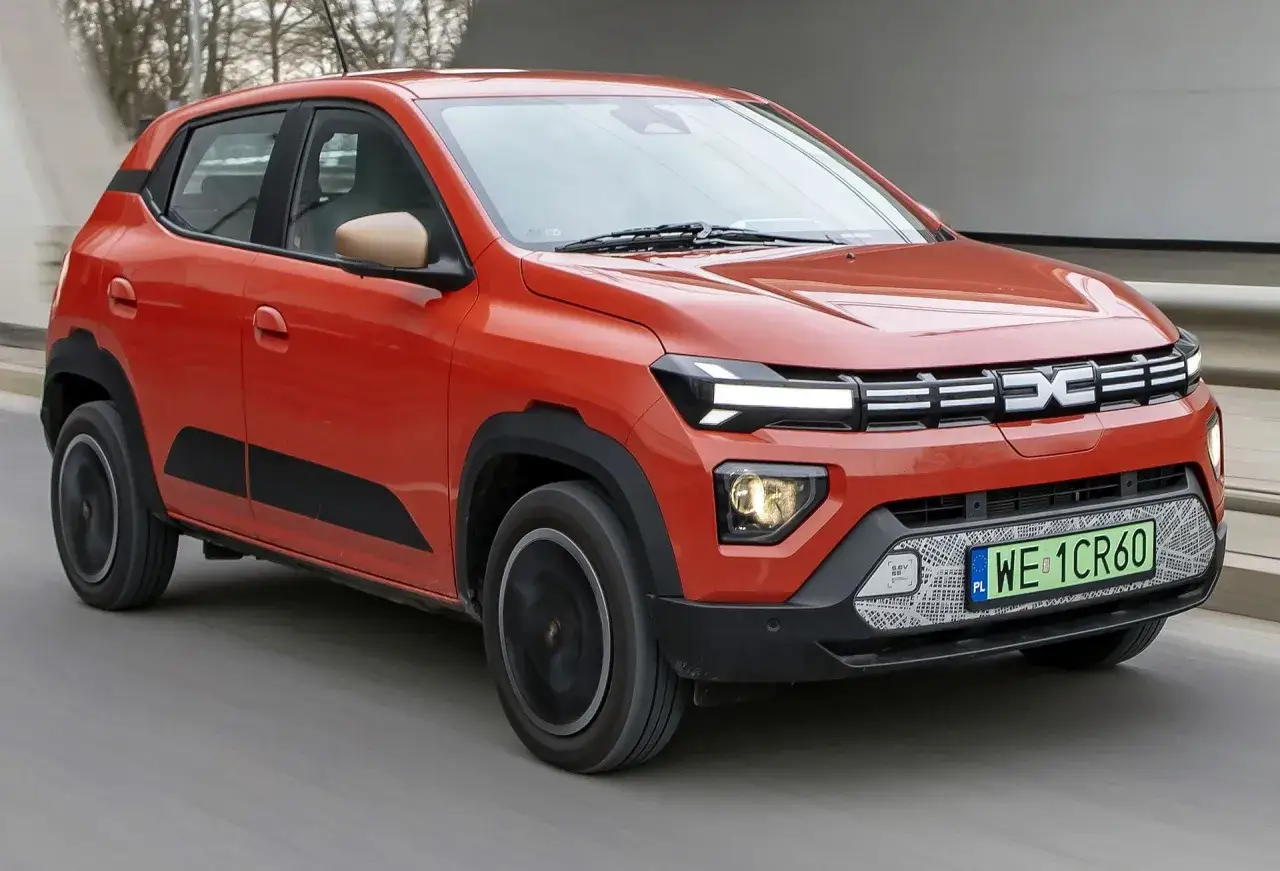 Pomarańczowy, tani samochód elektryczny Dacia Spring jedzie po drodze.